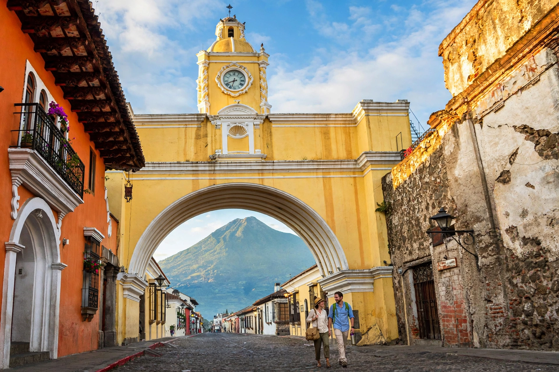The yellow Santa Catalina Arch in Antigua, Guatemala with Volcan de Agua towering behind the colonial rooftops
