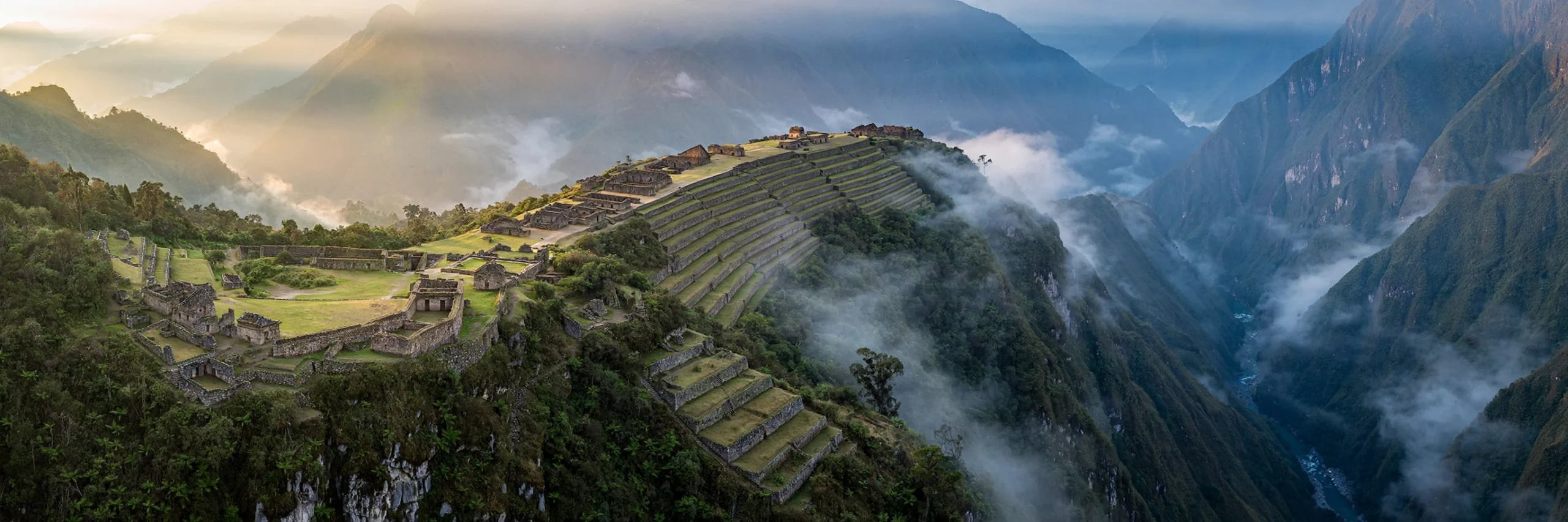 Wide view of Choquequirao Inca ruins spread across a green mountain ridge above the Apurimac canyon in Peru
