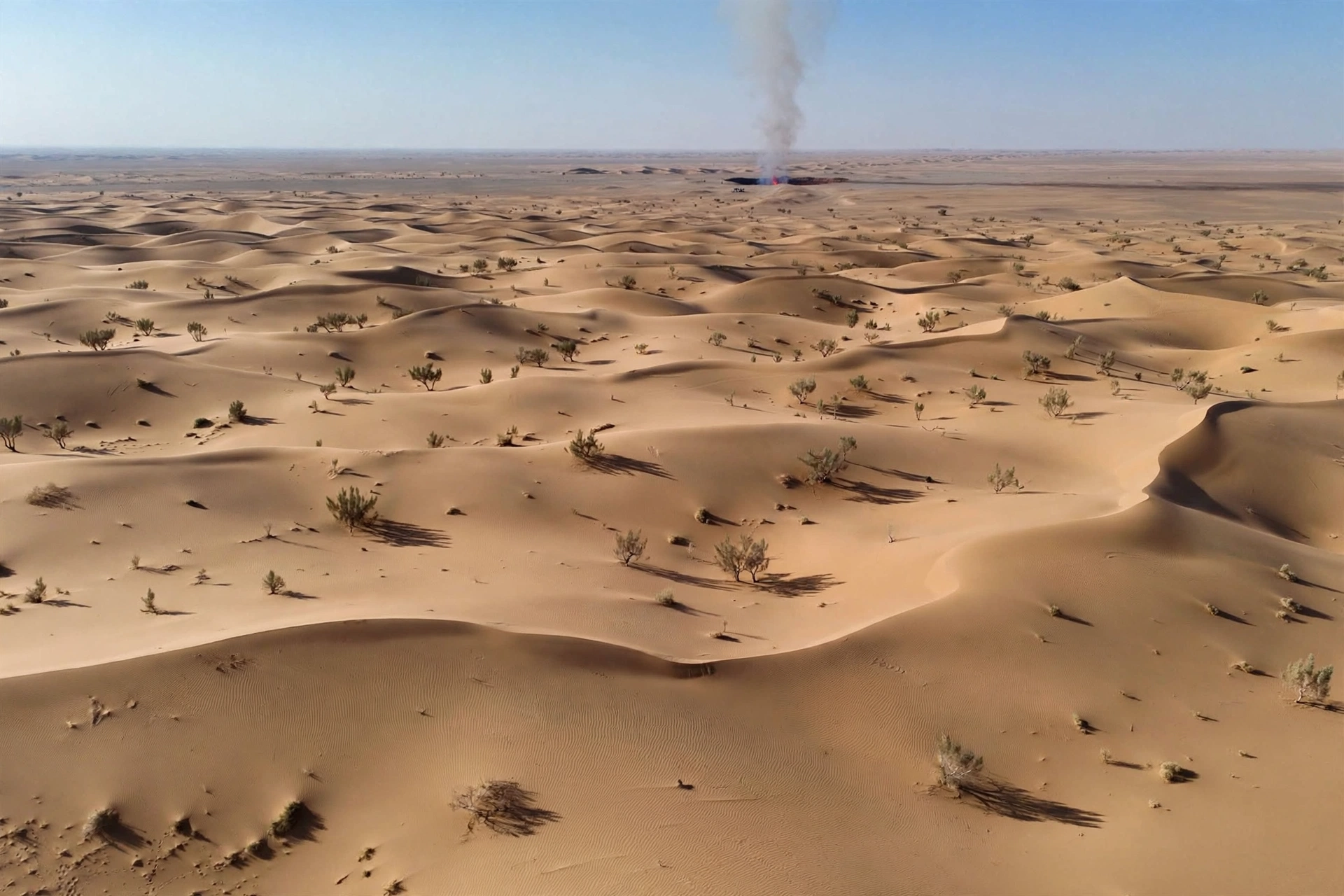 Aerial view of the Karakum Desert with smoke rising from the distant Darvaza crater