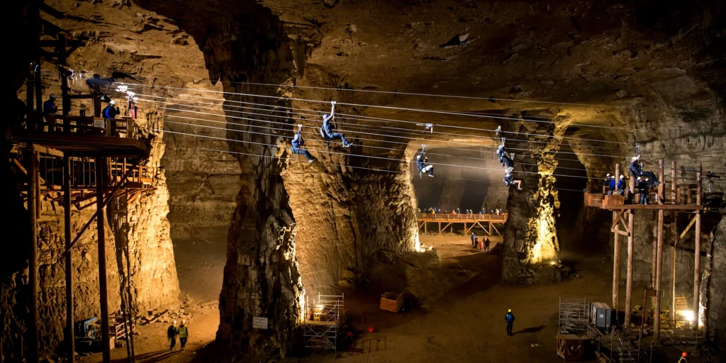 A vast limestone cavern at Louisville Mega Cavern, Kentucky, with zipline cables crossing a huge underground space lit by warm spotlights