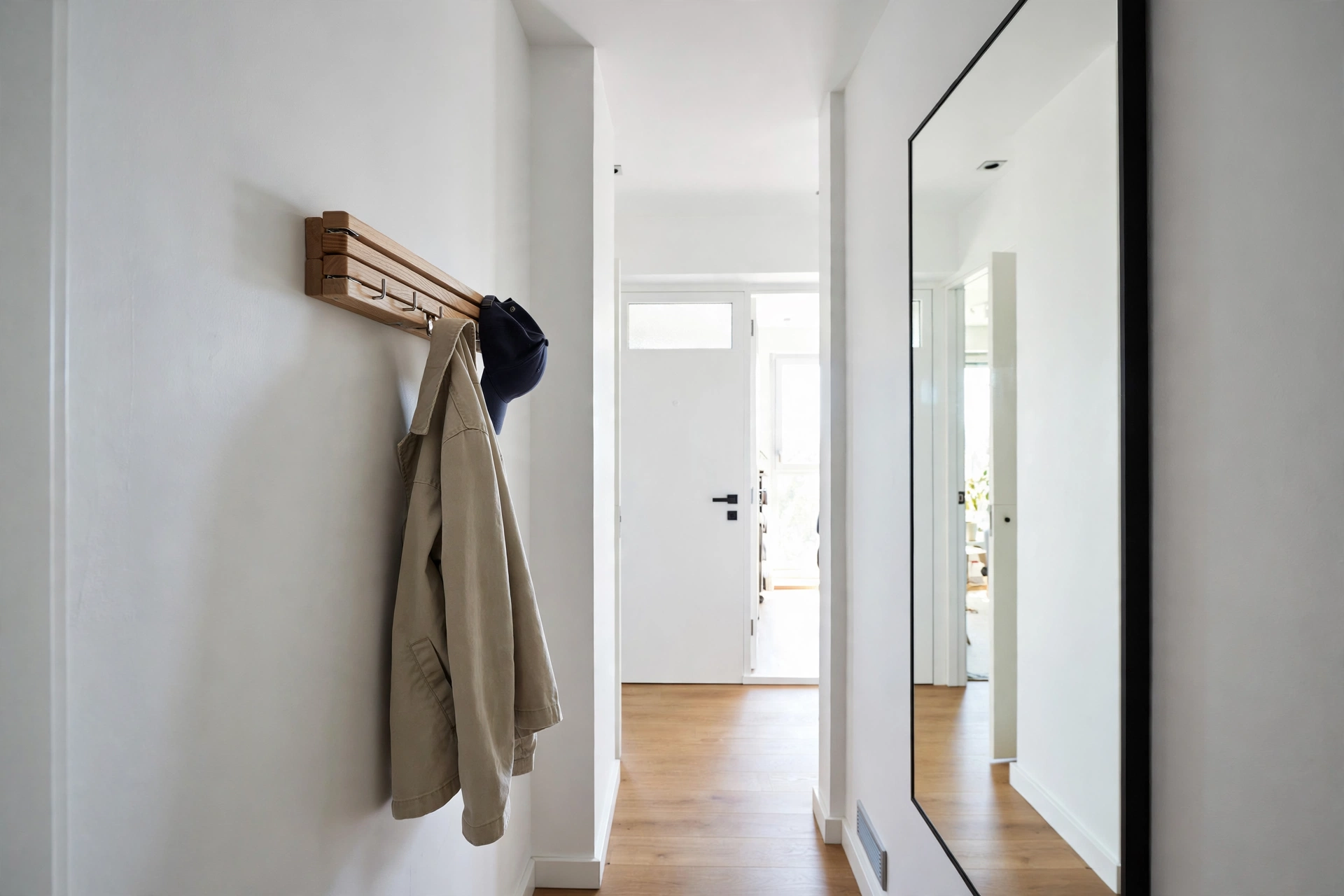Narrow apartment hallway with slim oak flip-down coat rack, hooks folded flat against the wall