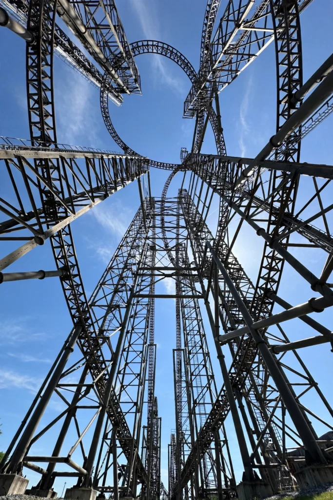 Looking up at a towering roller coaster structure against a blue sky