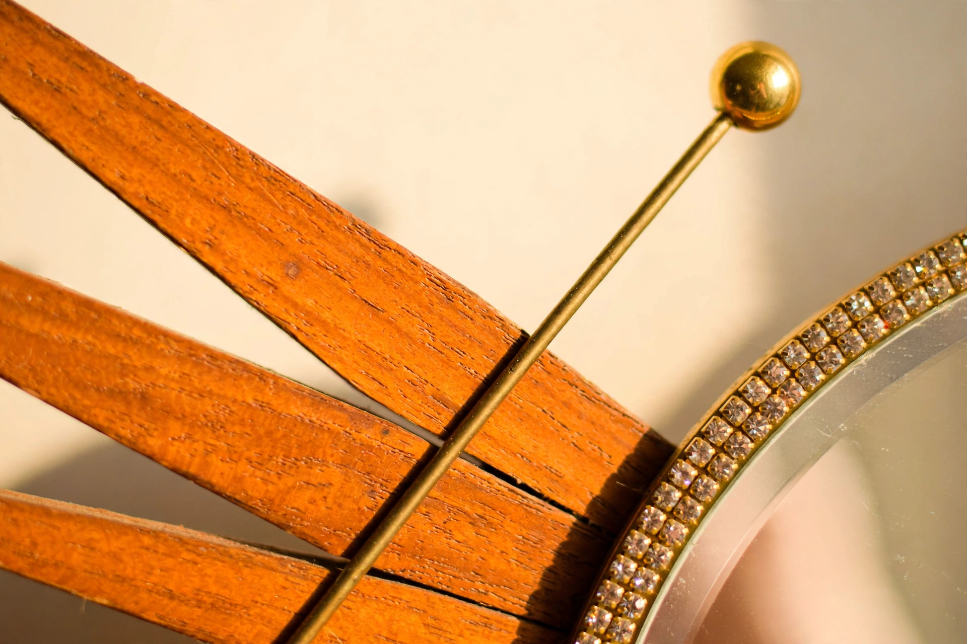 Close-up of the handmade mid-century starburst mirror showing wooden rays, brass rod, gold sphere and crystal-studded ring